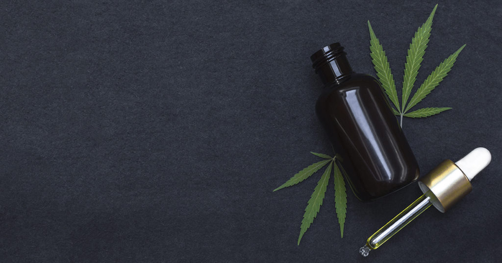 A small tincture bottle with cannabis leaves on a black backdrop