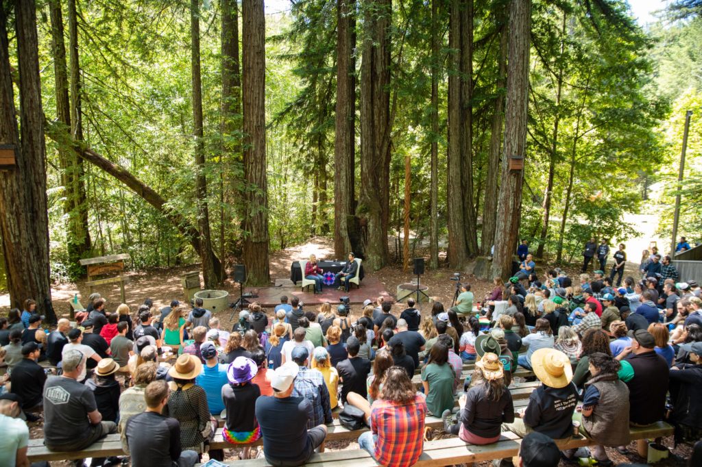 Capture of the keynote at Meadowlands 2018; two speakers in front of a large audience in an outdoor venue in the middle of a forest of trees about cannabis