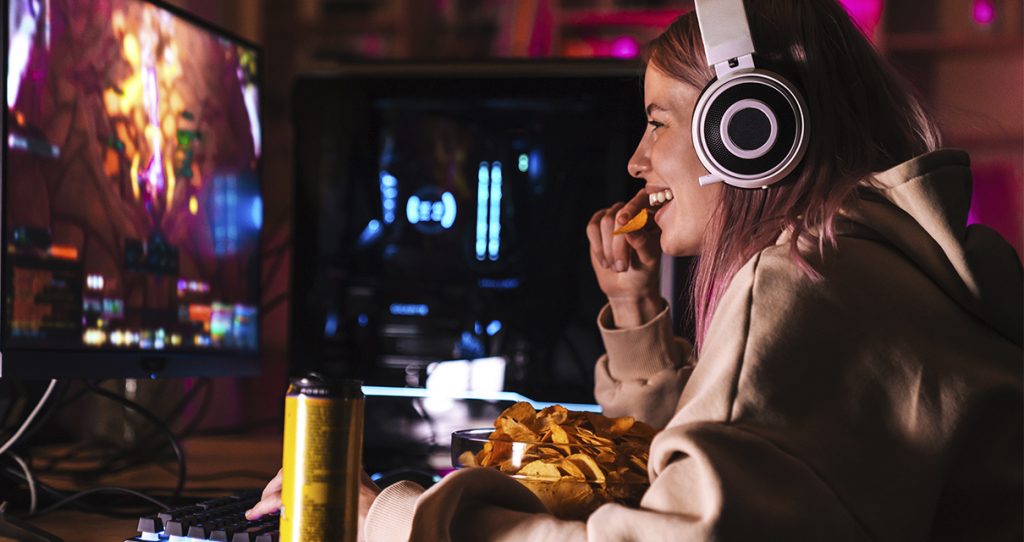 Girl with gaming headset watching an esports game on computer monitor while eating a snack about the three e's